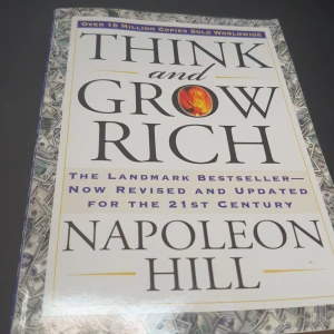 Think and Grow Rich Napoleon Hill - Säljer boken 'Think and Grow Rich' av Napoleon Hill. Denna klassiska bästsäljare har reviderats och uppdaterats för 2000-talet. Omslaget är dekorerat med ett mönster av sedlar och en flammande symbol. Perfekt för dig som vill utveckla ditt tänkande och nå framgång.