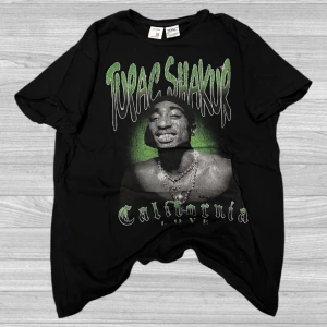 Bershka T-Shirt (Tupac Shakur)  - Cool svart T-shirt från Bershka med ett stort tryck av Tupac Shakur i grönt och vitt. Perfekt för dig som vill ha en avslappnad och stilren look med en touch av hiphop-kultur. T-shirten har korta ärmar och en rund halsringning.