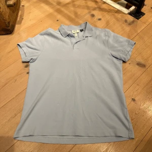 Ljusblå pikétröja från H&M Essentials - Säljer en stilren ljusblå pikétröja från H&M Essentials. Tröjan har en klassisk krage och korta ärmar, perfekt för en avslappnad look. Tillverkad i ett mjukt material som känns skönt mot huden. Storlek 175