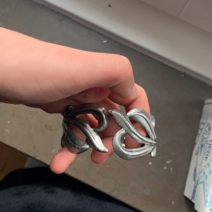 Silverfärgat armband med organiskt mönster - Unikt armband i silverfärg med ett flätat, organiskt mönster. Armbandet har en bred och robust design som ger ett statement-intryck. Perfekt för dig som gillar smycken med konstnärlig känsla.