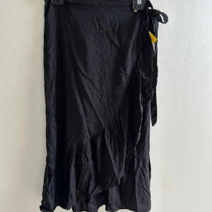 Svart omlottkjol från Pernilla Wahlgren - Säljer en svart omlottkjol från Pernilla Wahlgren. Kjolen har volang nertill och knyts i midjan. Den är oanvänd. Passar perfekt till sommaren🩷🩷