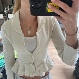 Vit volangkofta från Ralph lauren - Säljer en vit kofta från Ralph lauren med dragkedja framtill och volangdetalj nedtill. Koftan har lång ärm, stor krage och är croppad i modellen. Perfekt för dig som gillar en feminin och trendig stil.