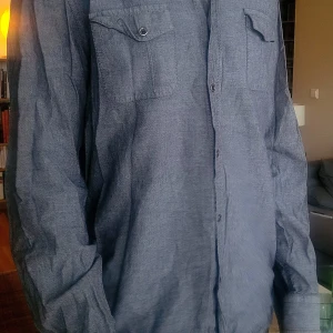 Blå-grå skjorta från DKNY Jeans - Säljer en stilren blå-grå skjorta från DKNY Jeans med två bröstfickor och knappar framtill. Skjortan har lång ärm och klassisk krage. Bra begagnat skick