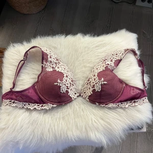 Superfin Intimissimi bh st 70B - Säljer en superfin vinröd Intimissimi bh med vackra vita spetsdetaljer och broderade blommor. Bh:n har justerbara axelband och en elegant design som ger en lyxig känsla. Säljer pga fel storlek. Storlek 70B