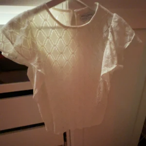 Vit spetsblus från Holly & Whyte - Säljer en söt vit blus från Holly & Whyte med korta ärmar och vackert spetsmönster. Blusen har rund halsringning och ett diskret strukturmönster i tyget. Pris kan diskuteras 