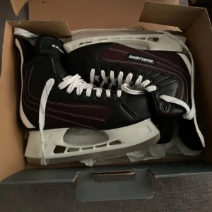 Bauer Flexlite 1.0 skridskor - Säljer ett par svarta Bauer Flexlite 1.0 skridskor med vita snören och vita skenor. Klassisk hockeymodell med robust konstruktion och snygga kontrastsömmar. Perfekta för isträning eller match.