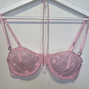 Rosa spets-bh  - Säljer en söt rosa bh med spets, halterneckdesign och hjärtformade detaljer. Bh:n har justerbara band och vanlig knäppning bak. Den är aldrig använd men tvättrådet är bortklippt