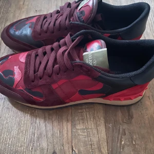 Valentino Rockrunner sneakers i röd camouflage - Säljer ett par Valentino Rockrunner sneakers med röd och svart camouflage-mönster. Skorna har vinröda mockadetaljer, svarta och röda partier. Skicket är som på bilderna och Skorna passar 27,5cm-28,5 längd under 27,5 kan vara litet men funkar om ni undrar varför jag säljer de så billigt så är de för att vem gillar inte snabba affärer alltså de är inget fel med varan tyvärr kommer ingen box men de är äkta enligt sicuro fashions äkta hands koll 