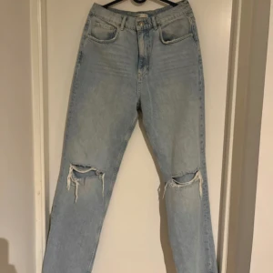 Ljusblå jeans med slitningar - Säljer ett par ljusblå jeans från Premium Denim med slitna detaljer vid knäna. Jeansen har klassisk femficksdesign, raka ben och normal passform. Perfekta för en avslappnad och trendig stil.