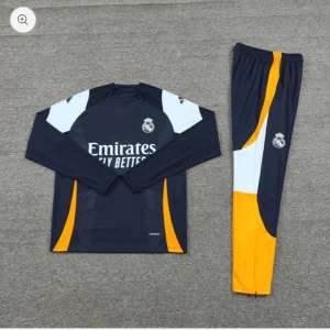 Real Madrid långärmad fotbollströja och byxor - Mörkblå långärmad fotbollströja med vita och orange detaljer från Real Madrid. Tröjan har klubbmärke och Adidas-logga, samt texten 'Emirates Fly Better' på bröstet. Matchande byxor i samma färger och material.