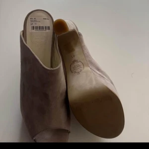 Ljusrosa mocka mules med klack från Novita - Säljer ett par ljusrosa mules från Novita i mjuk mocka. Skorna har öppen tå, klack och en stilren design som passar till många outfits. Perfekta för dig som gillar en elegant men enkel look. Skorna är helt nya och oanvända!! Storlek 41 men passar mig som vanligtvis har stlk 39.