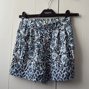 Blommiga shorts från H&M - Snygga shorts med blått och vitt blommönster från H&M. De har elastisk midja och är tillverkade i ett mjukt bomullsmaterial. Perfekta för varma dagar och ger en fräsch sommarkänsla.