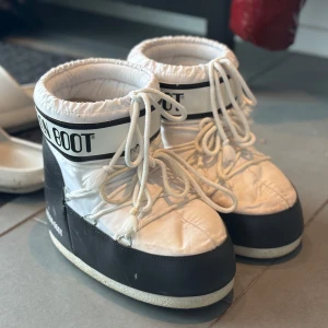Svarta och vita Moon Boot snowboots - Säljer ett par klassiska Moon Boot snowboots i svart och vitt med tydlig logga runt skaftet. Skorna har snörning framtill och en vadderad, quiltad ovandel som håller fötterna varma under vintern. Perfekta för snöiga dagar. Just nu är de lite skitiga men vid köp så tvättar jag de så bra som det går!❤️