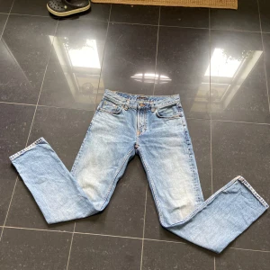 Ljusblå jeans från Nudie Jeans - Säljer ett par klassiska ljusblå jeans från Nudie Jeans med raka ben och femficksmodell. Jeansen har orange sömmar och subtil slitning för en avslappnad look. Perfekta för dig som gillar tidlös denimstil.