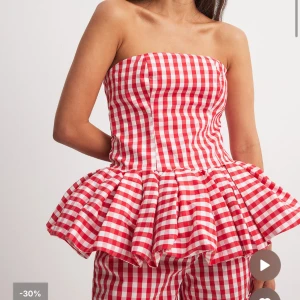 Röd och vit rutig tubtopp med volang - Superfin tubtopp i röd och vit rutig bomull med volang nertill. Toppen har en ballongliknande siluett och är axelbandslös, perfekt för en somrig look. Säljer då den inte kommer till användning längre.