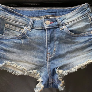 Blå lågmidjade jeansshorts stl 36 - Snygga blå jeansshorts med fransiga kanter och klassisk femficksdesign. Shortsen har låg midja .  36 cm  mätt rakt över 