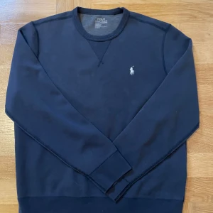 Mörkblå sweatshirt från Polo Ralph Lauren - Säljer en klassisk mörkblå sweatshirt från Polo Ralph Lauren med rund halsringning och broderad logga på bröstet. Tröjan har långa ärmar och är perfekt för en avslappnad stil.