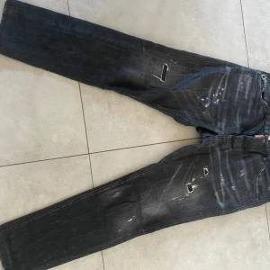 Svarta jeansbyxor från Dsquared2 - Säljer ett par svarta jeansbyxor från Dsquared2 med slitna detaljer och distressed look. Byxorna har raka ben och klassisk femficksdesign. Perfekta för dig som gillar en edgy stil.
