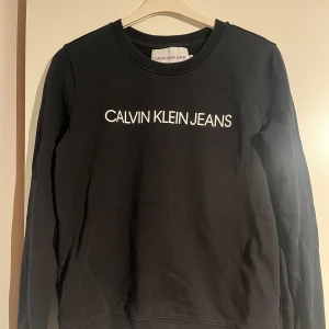 Svart sweatshirt från Calvin Klein Jeans - Svart sweatshirt från Calvin Klein Jeans med vit logotyp framtill. Endast använd ett fåtal gånger 