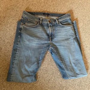 Ljusblå jeans Lean Dean från Nudie Jeans - Säljer ett par ljusblå Lean Dean jeans från Nudie Jeans. Klassisk femficksmodell med orange sömmar och broderade bakfickor. Jeansen är i stretchig bomull med smal passform och normal midja.