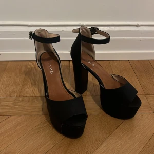 Svarta platåklackar med öppen tå och ankelrem - Säljer ett par svarta platåklackar från Tiamo med hög blockklack, öppen tå och justerbar ankelrem med spänne. Stl 39