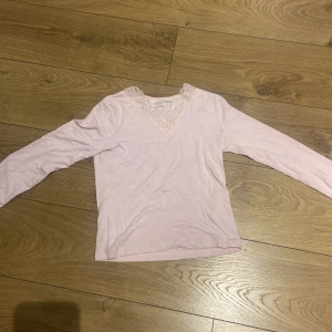 Ljusrosa långärmad topp med spetsdetalj - Säljer en ljusrosa långärmad topp med v-ringning och fina spetsdetaljer runt halsen. Perfekt för dig som gillar en söt och feminin stil. Mjuk och skön att ha på sig. Säljer den för att den är för liten köpte i fel storlek och glömde ta kvitto använd 2 gånger och är mycket fin och skön 