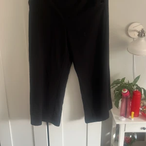 Svarta byxor från Vila - Svarta byxor från Vila med resår i midjan och croppad längd. Byxorna har en enkel och stilren design som passar till många olika outfits. Perfekta för dig som gillar bekväma och snygga byxor.