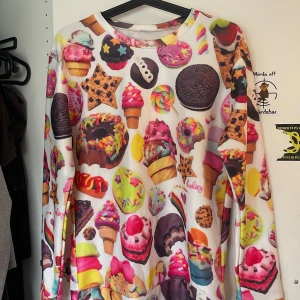 Färgglad sweatshirt med godistryck - En långärmad sweatshirt med färgglatt tryck av glass, kakor, godis och bakverk. Tröjan har rund hals och är i mjukt material, perfekt för dig som gillar unika och lekfulla plagg.