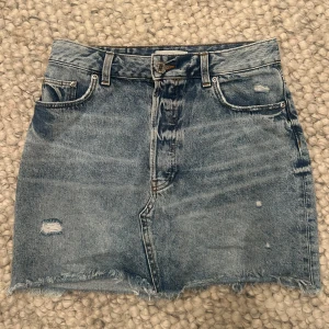 Blå jeanskjol med rå kant - Säljer snygg och trändig low waist jeanskjol med slitna detaljer 