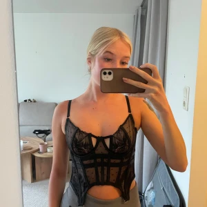 Svart spetskorsett med meshdetaljer - Säljer en svart korsett med spets och meshdetaljer. Toppen har smala justerbara axelband. Aldrig använd endast testad. Storlek 80B men passar mig som vanligtvis har 75B 