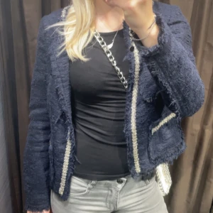 Mörkblå elegant kofta - Säljer en mörkblå kofta/tröja från Zara med dekorativa silverfärgade detaljer längs kanterna. Den har fyra fickor framtill och är tillverkad i ett strukturerat tyg som ger en exklusiv känsla. Perfekt för att lyfta vilken outfit som helst. Nästan helt oanvänd så ser som ny ut. Den är i storlek xs.