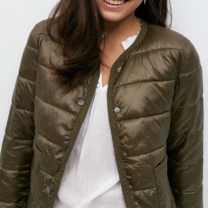 Tunn dunjacka från Gina  - Säljer en olivgrön pufferjacka från Gina med rund halsringning och tryckknappar framtill. Jackan har två stora fickor och quiltad design. Perfekt för lager-på-lager och enkel att styla till jeans eller kjol. Storlek 158/164 men passa mig med XS😊