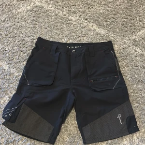 Pelle P shorts - Säljer ett par ”Pelle P” shorts i storlek M, som sitter normalt i storlek. De är i nyskick och ny pris är 1500 kr. De består av ett starkt och slittåligt material och många fickor, både med och utan dragkedja. Bälte följer även med till de. 
