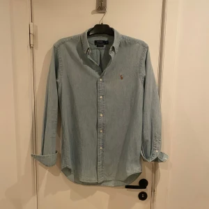 Ljusblå skjorta från Ralph Lauren - Säljer en stilren ljusblå skjorta från Ralph Lauren. Skjortan har långa ärmar och knappar framtill. Den är tillverkad i bomull och har en klassisk passform med en broderad logotyp på bröstet. Storlek s men passar M perfekt. 