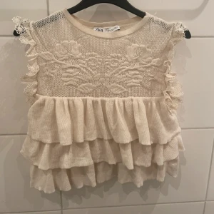 Beige blus med spets och volanger  Zara - Beige blus från Zara med spetsdetaljer och volanger. Lite glittrig i tyget som syns på andra bilden! Storlek S men liten i storleken!