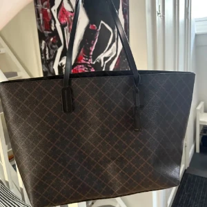 By Marlane Birger väska - Snygg brun shoppingväska med rutigt mönster och långa handtag. Perfekt för att bära med sig allt man behöver under dagen. Stilren och praktisk design. 