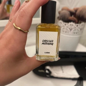 Chelsea Morning parfym från Lush - Säljer en flaska Chelsea Morning parfym från Lush. Flaskan är rektangulär med en svart kork och etikett med texten 'Chelsea Morning'. Parfymen har en gyllene färg och kommer i en stilren design.