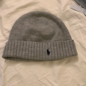 Grå stickad beaniemössa från Polo Ralph Lauren - Snygg grå stickad mössa från Polo Ralph Lauren med broderad logga framtill. Perfekt för kyliga dagar med sin mjuka och bekväma passform. Nypris ca 800, mitt pris: 250. Pris är inte hugget i sten, skriv vid minsta intresse