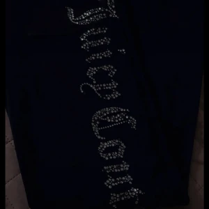 Svarta byxor från Juicy Couture med strass - Snygga svarta byxor från Juicy Couture med glittrande strassdetaljer längs benet. Perfekta för att ge en touch av glamour till din outfit.