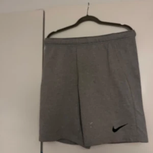 Grå träningsshorts/mjukisshorts från Nike - Säljer ett par grå träningsshorts från Nike med Dri-FIT-teknologi. Shortsen har en elastisk midja och är perfekta för träning. De är tillverkade i ett mjukt och bekvämt material.