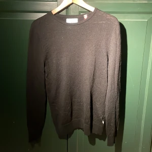 Svart merinoull tröja från Kronstadt - Säljer en stilren svart tröja från Kronstadt. Tröjan har en klassisk design med långa ärmar och rund halsringning. Perfekt för en avslappnad och snygg look. Den sitter som S men är lite tajtare i ärmarna. Lite nopprig. 