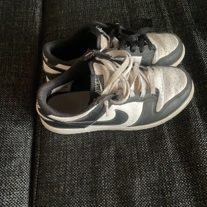 Nike Dunk i svart och vit - Säljer ett par klassiska Nike Dunk sneakers i svart och vit. Skorna har en stilren design med snörning och perforerade detaljer på tån för extra ventilation. Perfekta för en sportig look.