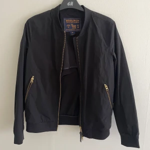 Bomberjacka Woolrich - Svart bomberjacka med gulddetaljer från märket Woolrich. Storlek M och i mycket fint skick!