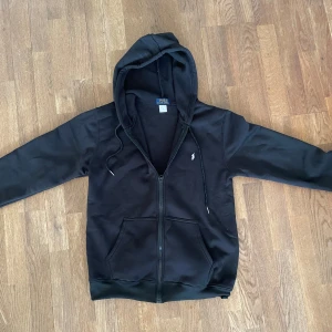 Svart hoodie storlek M - Säljer denna zip up tröjan då den inte passar mig. Jag har endast testat på mig den 1 gång. Pris kan diskuteras men vill helst inte gå mindre än 200kr