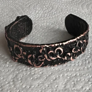 Svart och kopparfärgat armband - Unikt armband i svart med kopparfärgade detaljer. Armbandet har ett vackert mönster av sammanflätade hjärtan och är öppet i designen för enkel justering. Perfekt för att ge en stilfull touch till din outfit.