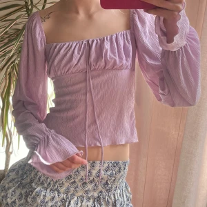 Ljuslila blus/ topp med långa ärmar - Säljer en söt ljuslila blus med långa ärmar och knytning framtill. Blusen har fyrkantig urringning och är tillverkad i ett lätt och luftigt material. Perfekt för vår och sommar! Sitter perfekt mot kroppen och framhäver en jätte fin form