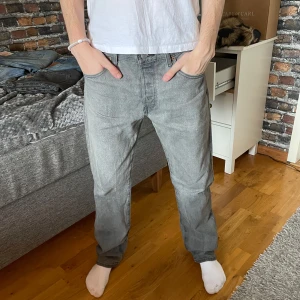 Levi's 501 jeans  - Snygga ljus grå jeans från Levi's med en klassisk femficksdesign. De har en rak passform och är perfekta för en avslappnad stil. Jeansen har en diskret tvättad look och en liten röd etikett på bakfickan. Modellen på jeansen är 501 