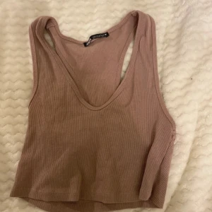 Rosa ribbad linnetopp från Zara - Säljer en snygg rosa ribbad linnetopp från Zara. Toppen har en djup urringning och är ärmlös, perfekt för varma dagar. Den är tillverkad i ett mjukt och stretchigt material som ger en bekväm passform.