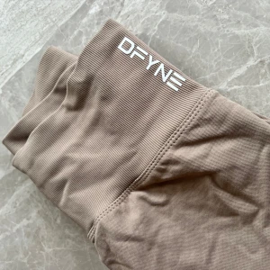 Beige leggings från DFYNE - Snygga beige leggings från DFYNE med hög midja och ribbad struktur. Perfekta för träning eller en avslappnad dag. Tillverkade i ett mjukt och stretchigt material för bästa komfort. Leggins är använda 1 gång i en timma så är i nyskick . Jag skulle säga att det är som storlek S något mindre kanske 