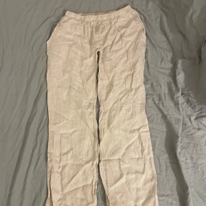 Beige linnebyxor från Chelsea Girls - Säljer ett par bekväma beige linnebyxor från Chelsea Girls. Byxorna har en elastisk midja för extra komfort och är tillverkade i 100% linne, vilket gör dem perfekta för varma dagar. Tillverkade i Italien. Lågmidjade 